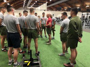 A group of ROTC cadets listen to an instructor in a large domed gym.