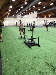 A ROTC cadet drags an exercise machine with weights along turf.