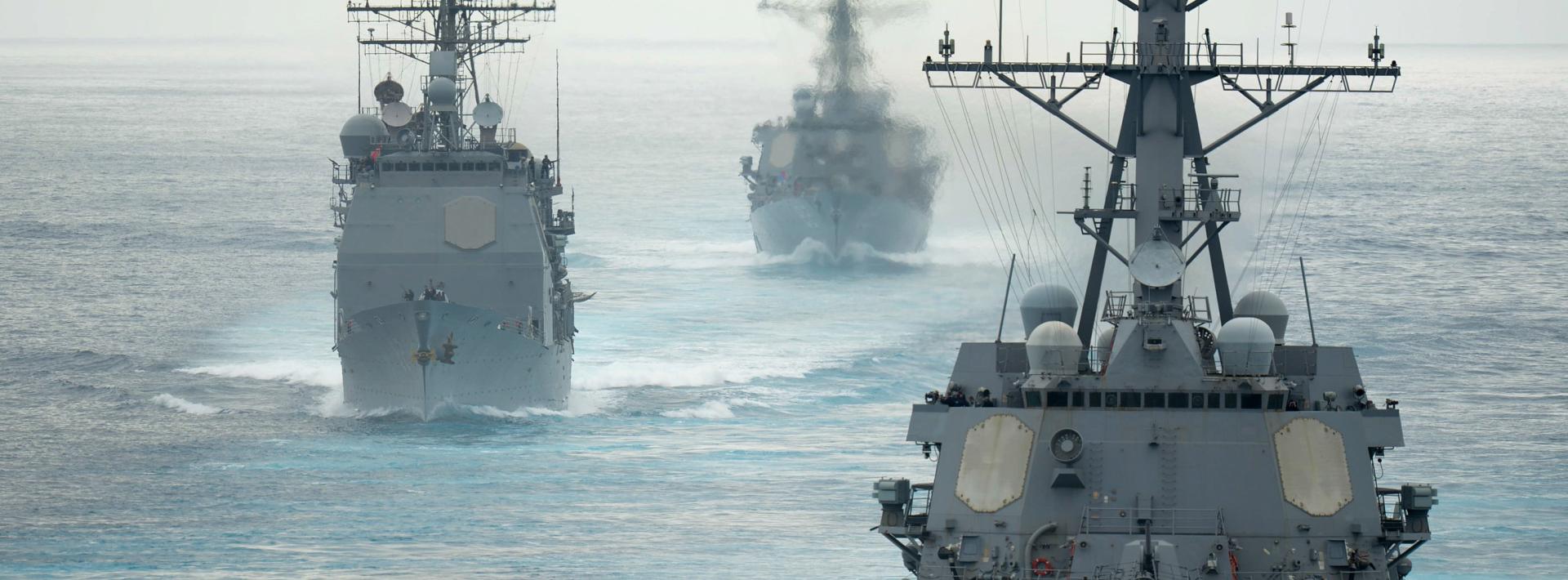 Three navy ships in formation on a large body of water.