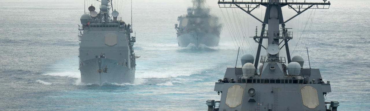 Three navy ships in formation on a large body of water.
